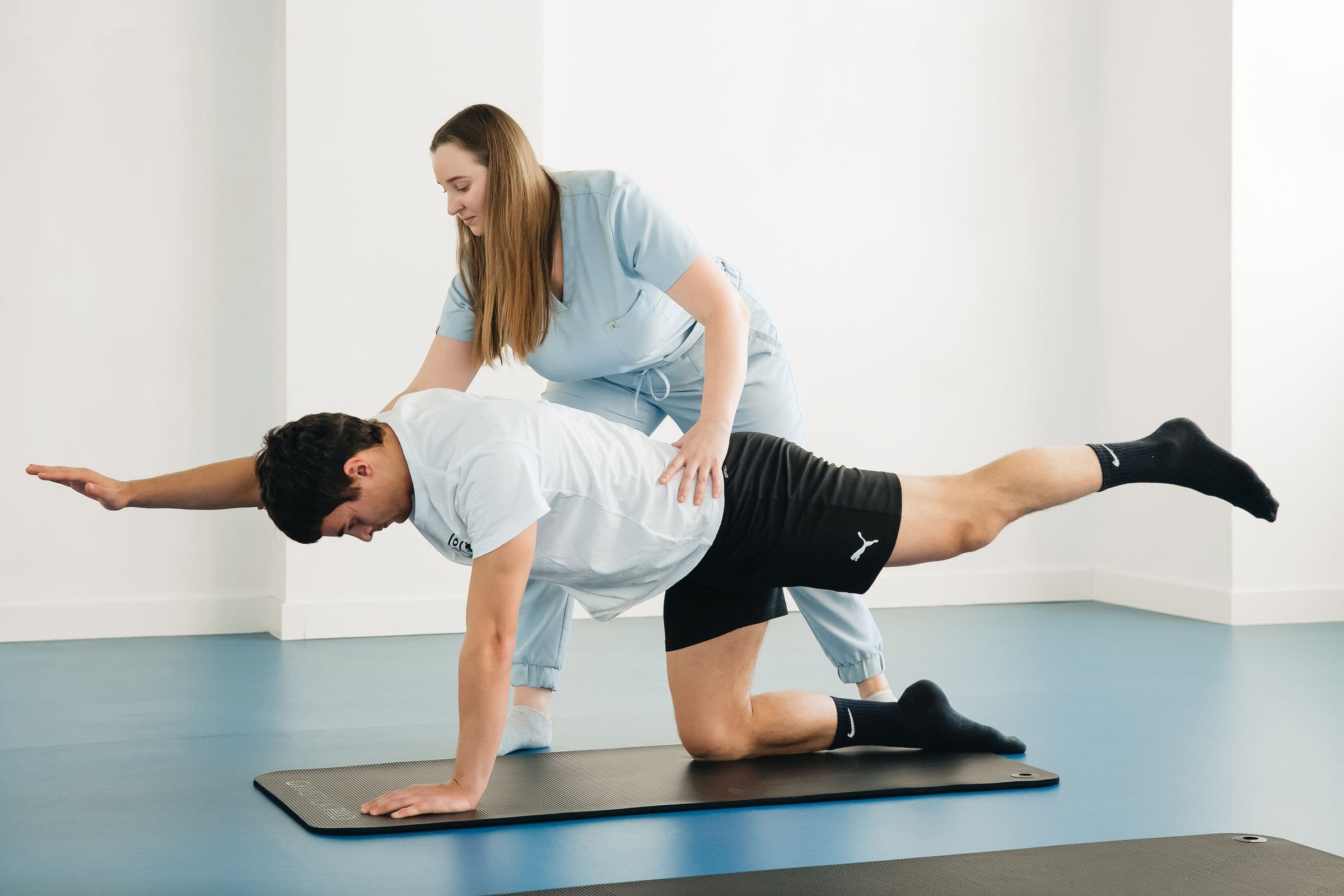 A physiotherapist guiding a patient through a balance exercise on a mat in a bright clinic