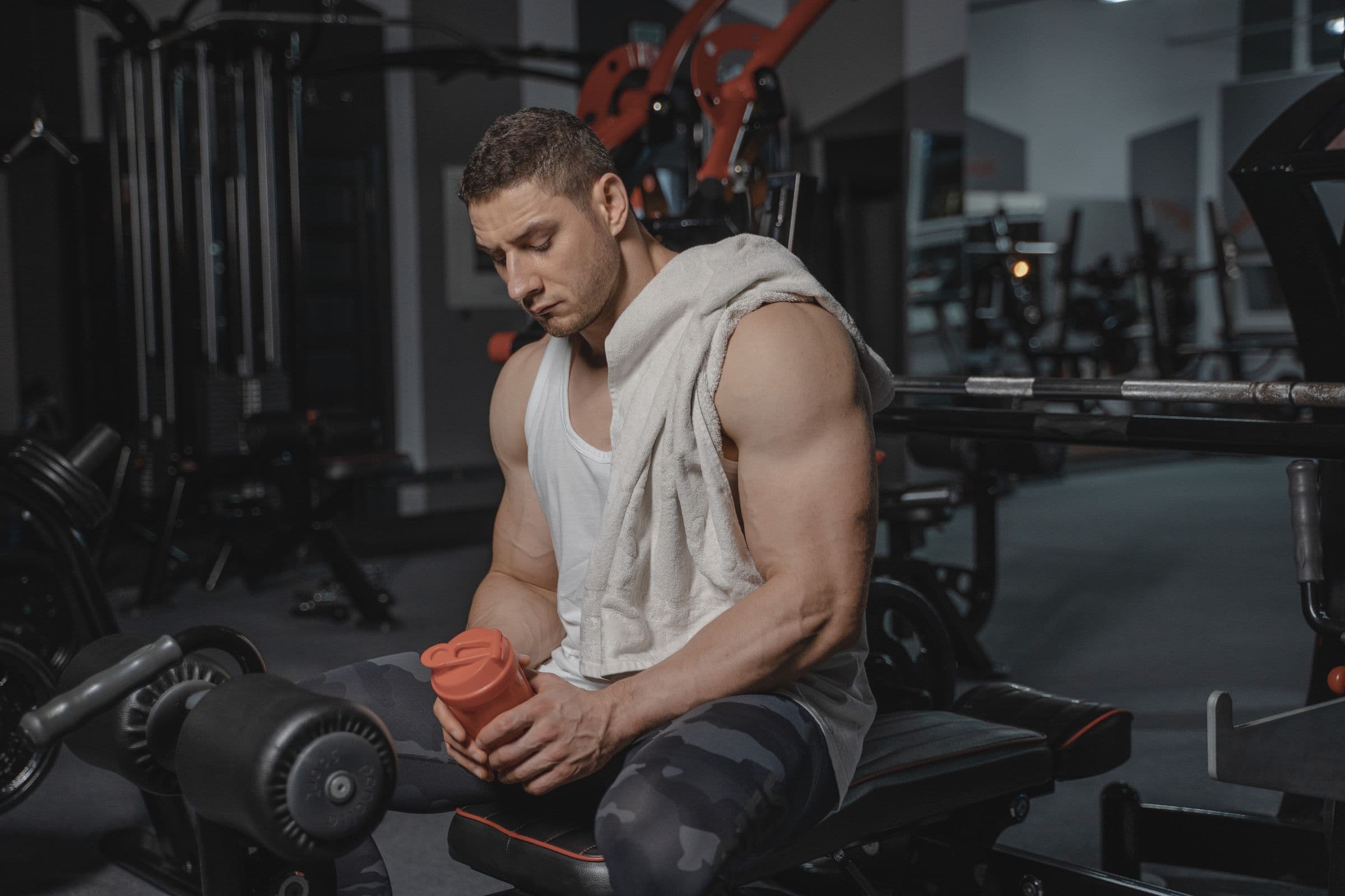 A man resting on a gym bench after a workout, holding a protein shaker