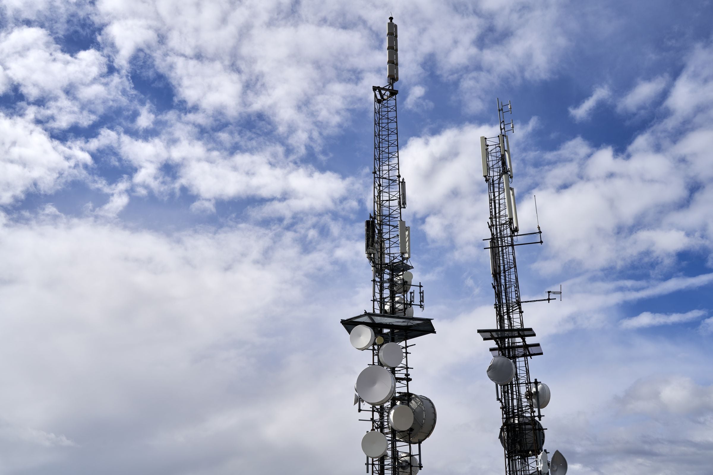 Telecommunication towers with antennas and dishes against a bright, cloudy sky