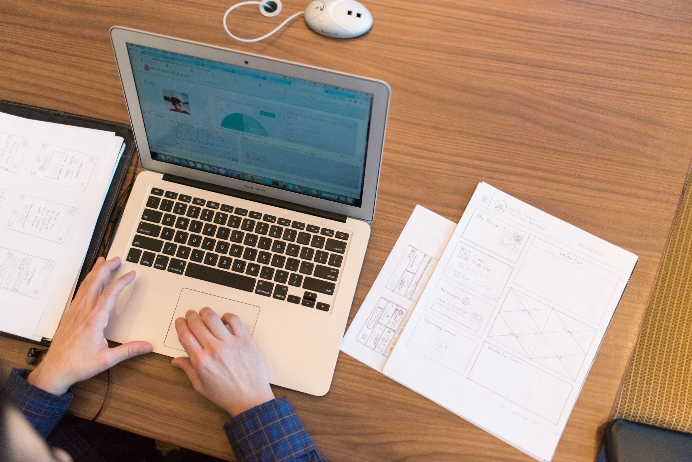 A designer working on a laptop with wireframe sketches